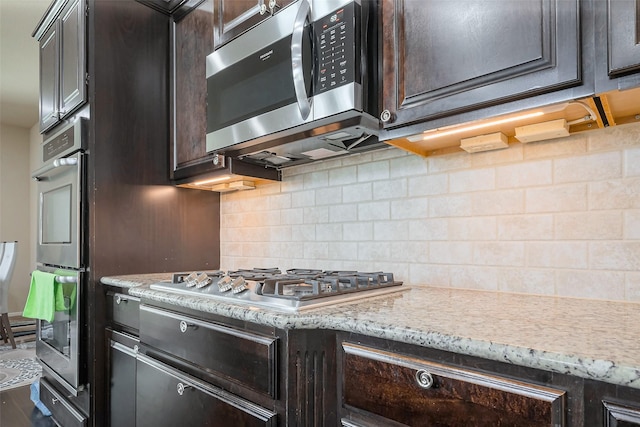 kitchen with stainless steel appliances, dark brown cabinets, light stone counters, and decorative backsplash