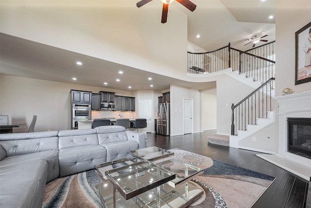 living area featuring ceiling fan, stairway, dark wood-type flooring, and a glass covered fireplace