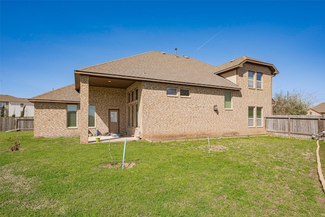 rear view of house with a fenced backyard, a yard, brick siding, and roof with shingles