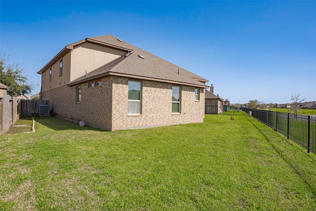 rear view of property featuring a yard, central AC unit, a shingled roof, and a fenced backyard