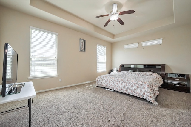 carpeted bedroom featuring ceiling fan, baseboards, and a raised ceiling