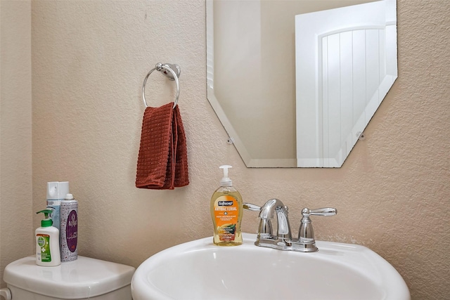 half bath with a textured wall and a sink