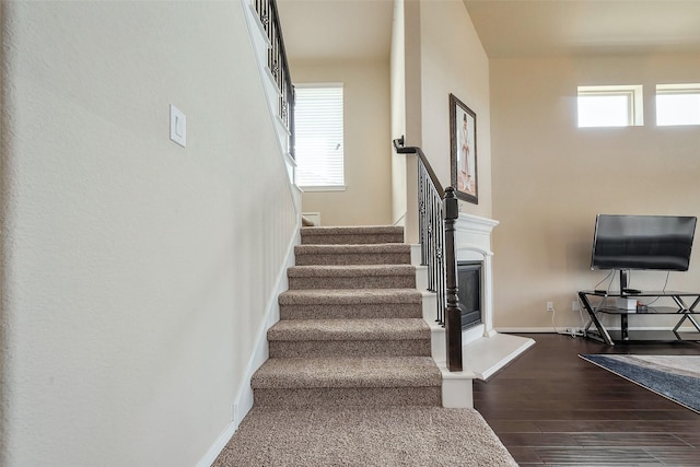 stairway with a fireplace with raised hearth, wood finished floors, and baseboards