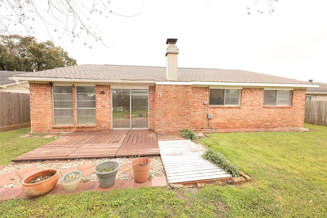 back of property with a deck, brick siding, fence, a lawn, and a chimney