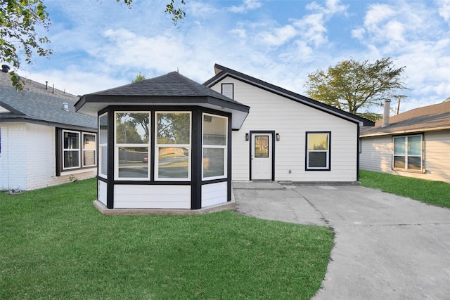 back of property with a yard, a shingled roof, a patio area, and a sunroom