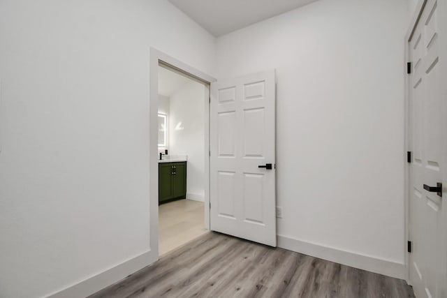 unfurnished bedroom with light wood-type flooring, baseboards, and ensuite bathroom