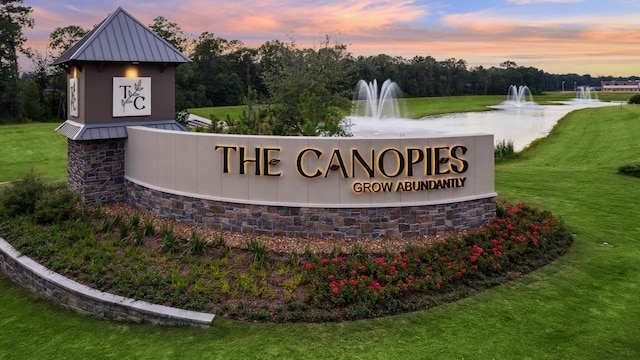 community / neighborhood sign featuring a lawn and a water view