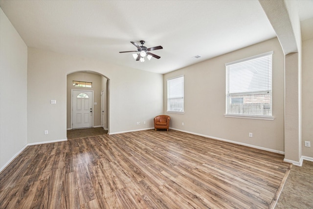 interior space with baseboards, visible vents, arched walkways, and wood finished floors