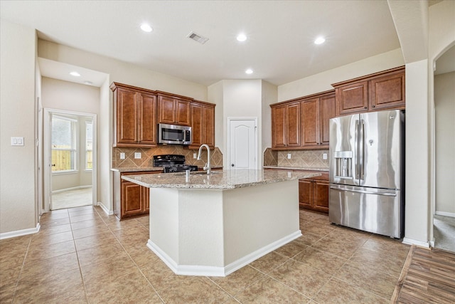 kitchen with brown cabinets, a center island with sink, stainless steel appliances, visible vents, and light stone countertops