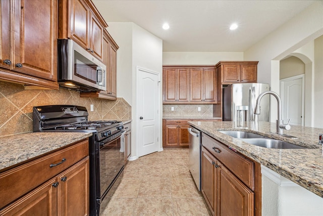 kitchen with decorative backsplash, appliances with stainless steel finishes, brown cabinets, light stone counters, and a sink