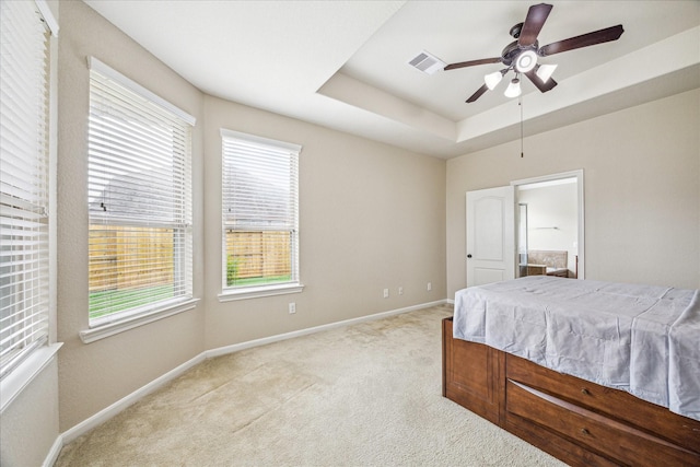 bedroom featuring light carpet, baseboards, visible vents, a raised ceiling, and ceiling fan