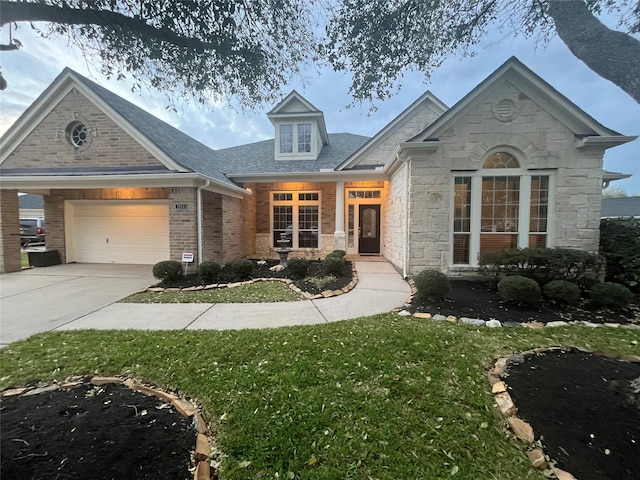 view of front facade featuring a garage, brick siding, driveway, stone siding, and roof with shingles