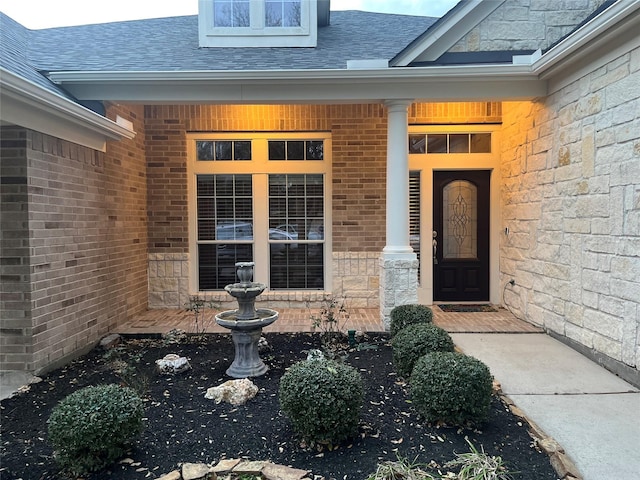 property entrance featuring a shingled roof, stone siding, brick siding, and covered porch