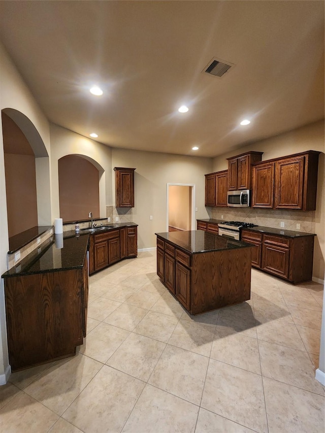 kitchen featuring visible vents, range with gas cooktop, stainless steel microwave, a center island, and a sink