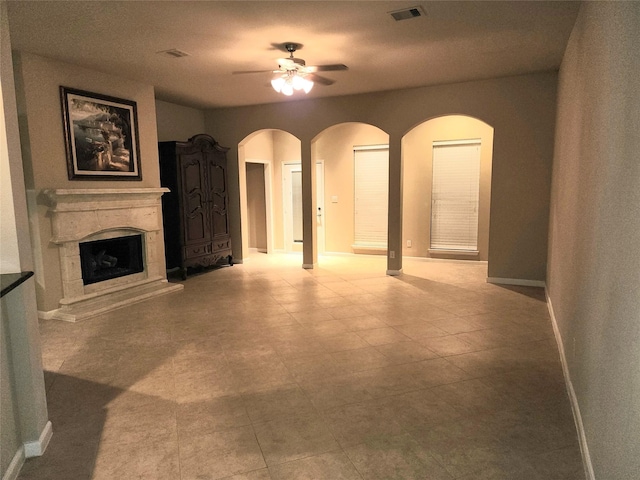 unfurnished living room featuring arched walkways, a premium fireplace, visible vents, baseboards, and a ceiling fan