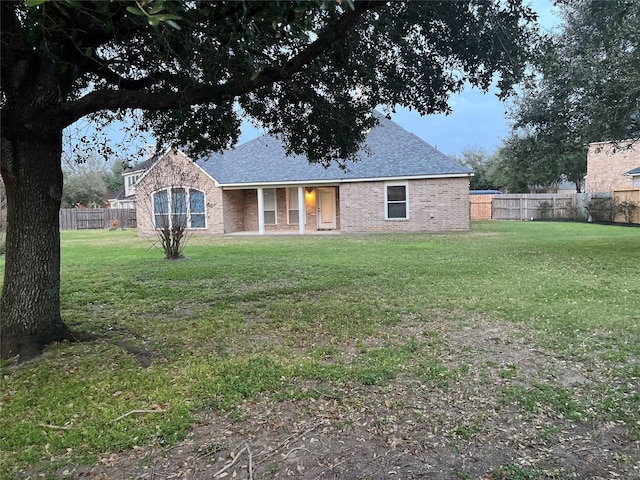 ranch-style home with a front lawn, a shingled roof, fence, and brick siding