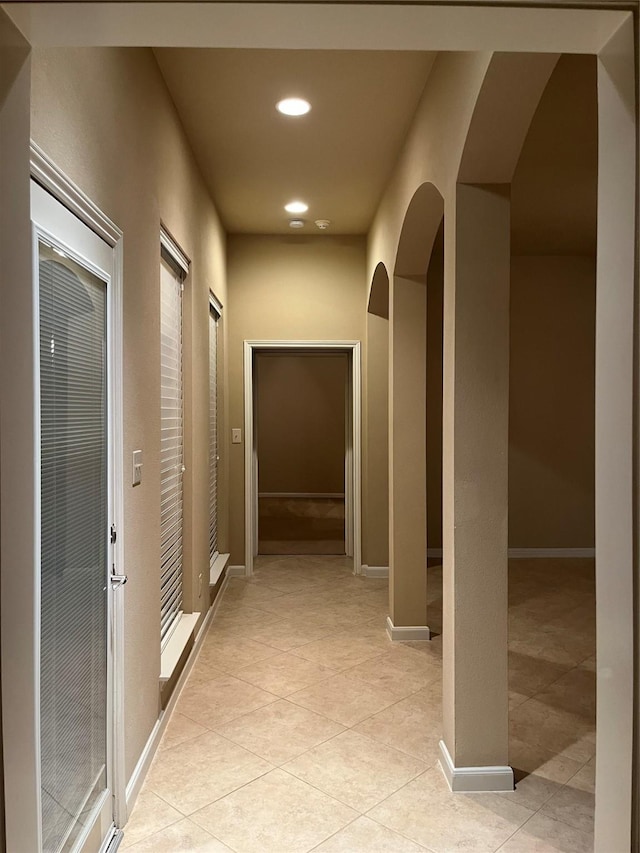 corridor featuring arched walkways, baseboards, recessed lighting, and light tile patterned floors