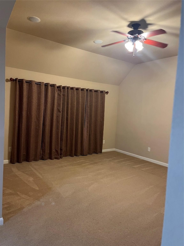 carpeted spare room featuring a ceiling fan, vaulted ceiling, and baseboards