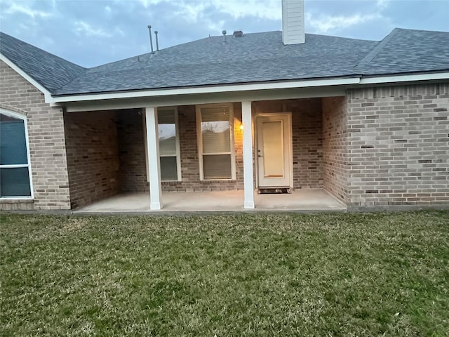 back of property featuring a yard, a patio, and brick siding