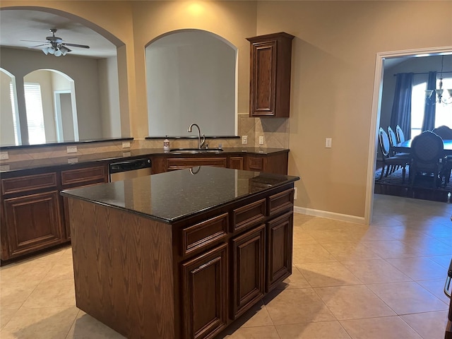 kitchen with tasteful backsplash, stainless steel dishwasher, light tile patterned flooring, a sink, and dark stone countertops