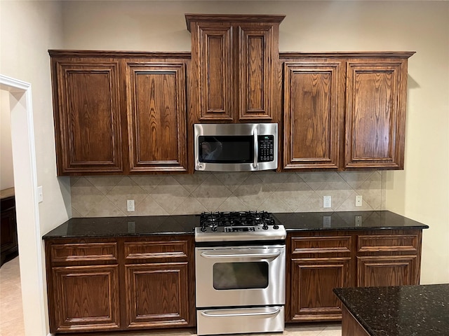 kitchen with stainless steel appliances, dark stone counters, backsplash, and dark brown cabinets