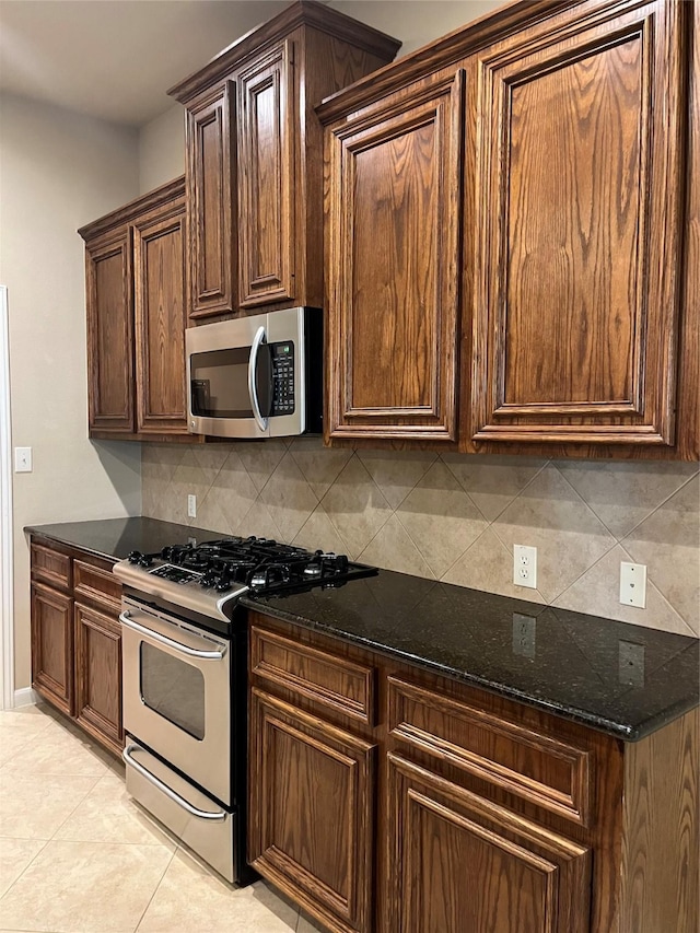 kitchen with light tile patterned floors, stainless steel appliances, dark brown cabinets, decorative backsplash, and dark stone counters