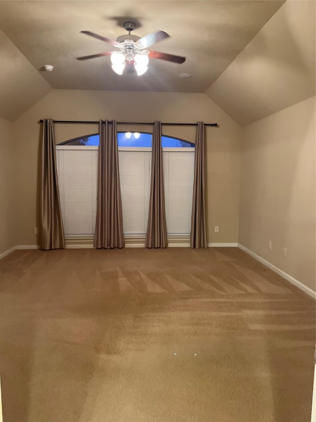 carpeted empty room with a ceiling fan, lofted ceiling, and baseboards