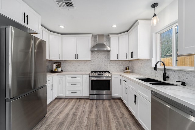 kitchen with visible vents, wall chimney exhaust hood, appliances with stainless steel finishes, wood finished floors, and a sink