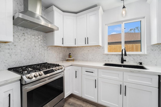 kitchen with decorative backsplash, stainless steel gas stove, a sink, wall chimney range hood, and white cabinetry