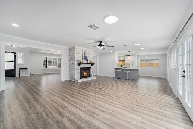 unfurnished living room with ornamental molding, a stone fireplace, wood finished floors, and visible vents