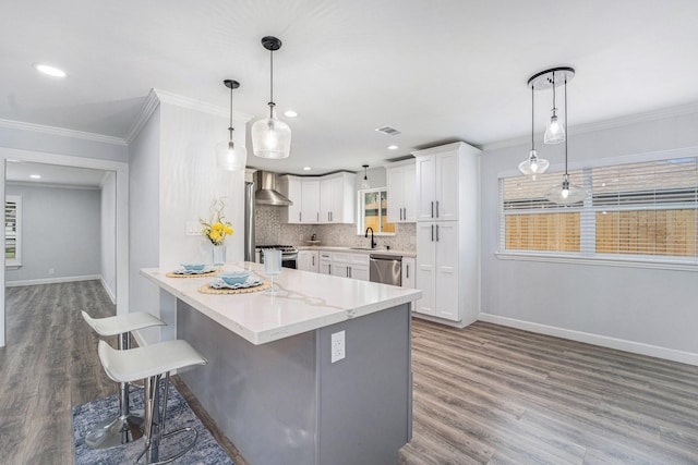 kitchen featuring decorative backsplash, a breakfast bar area, wood finished floors, wall chimney range hood, and white cabinetry