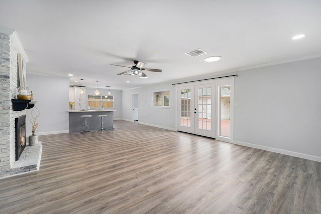 unfurnished living room featuring visible vents, wood finished floors, crown molding, french doors, and a fireplace