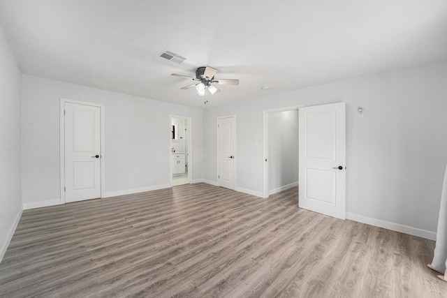 unfurnished bedroom with ensuite bathroom, wood finished floors, a ceiling fan, visible vents, and baseboards