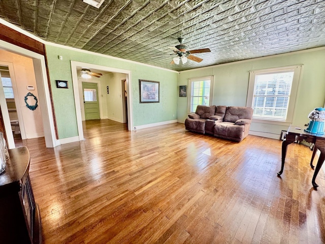 living room featuring an ornate ceiling, crown molding, wood-type flooring, a ceiling fan, and baseboards