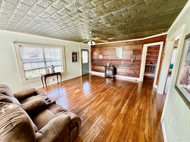 living area featuring an ornate ceiling, crown molding, a wood stove, baseboards, and hardwood / wood-style flooring