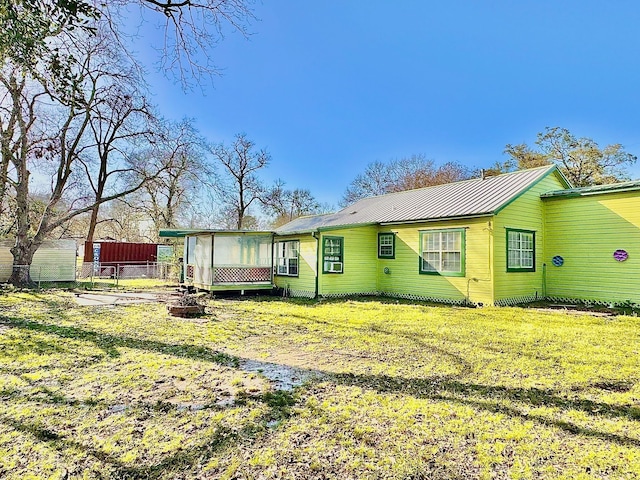 rear view of property featuring fence, metal roof, and a lawn