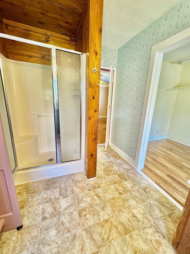 full bath with baseboards, a shower stall, a textured ceiling, and wallpapered walls