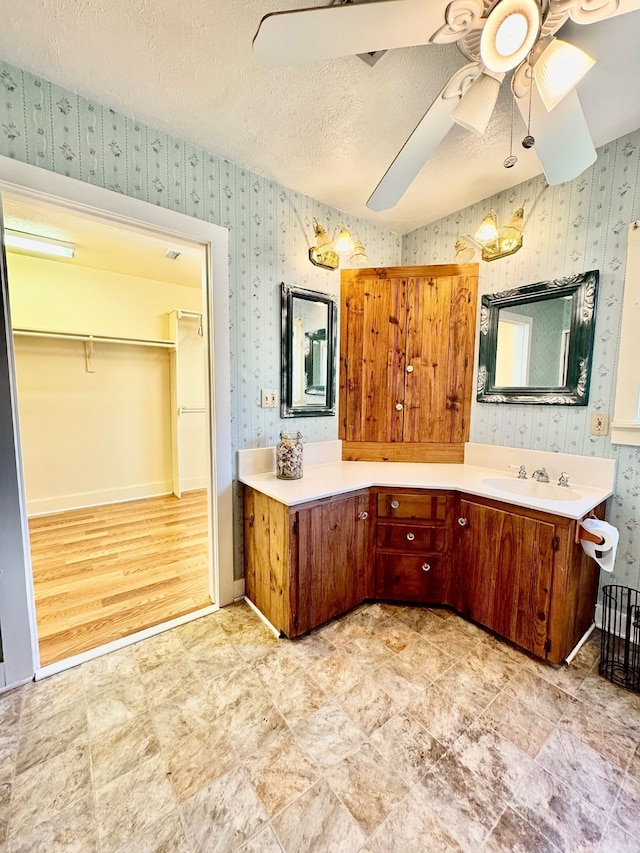 full bathroom with a textured ceiling, vanity, baseboards, a ceiling fan, and wallpapered walls