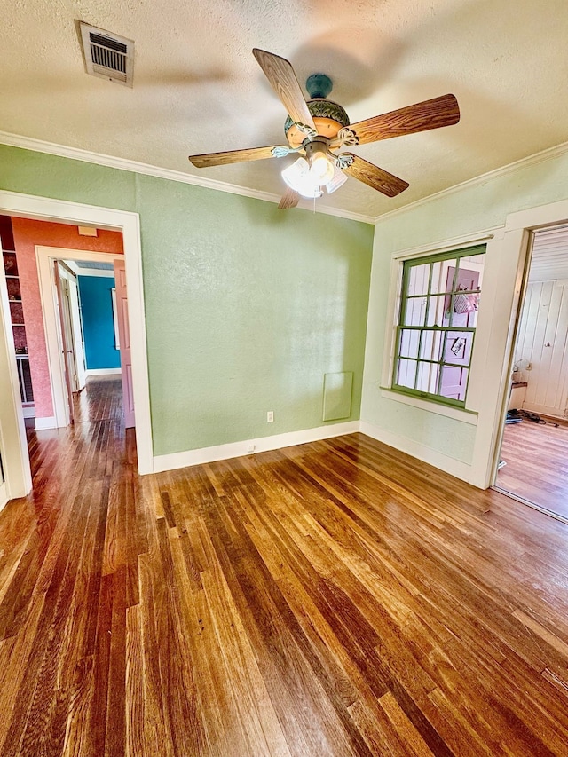 unfurnished room with crown molding, visible vents, a textured ceiling, wood finished floors, and baseboards