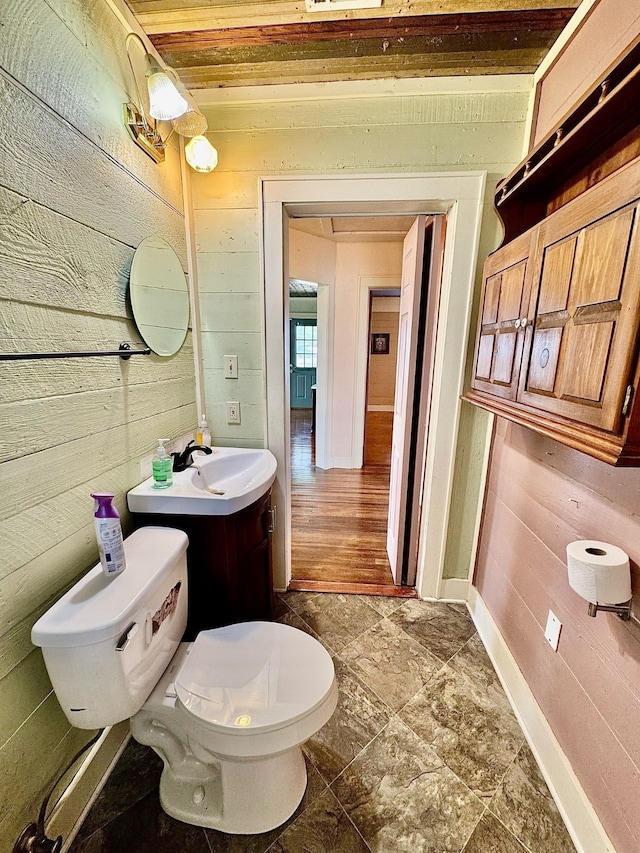 bathroom featuring wood walls, vanity, toilet, and baseboards