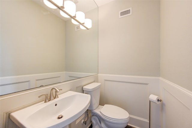 bathroom with toilet, a notable chandelier, a wainscoted wall, a sink, and visible vents