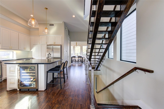 kitchen with white cabinets, stainless steel fridge with ice dispenser, dark countertops, wine cooler, and a kitchen bar