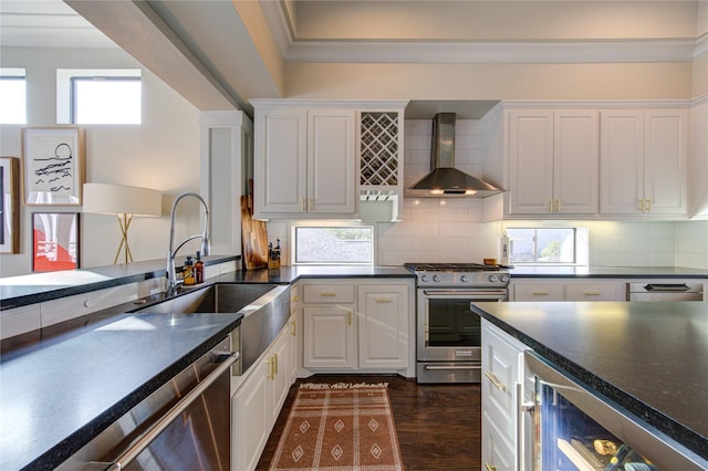 kitchen featuring dark countertops, wine cooler, stainless steel appliances, wall chimney range hood, and a sink