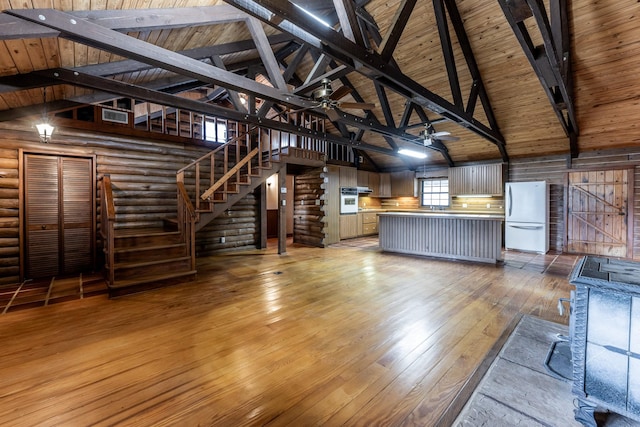 unfurnished living room featuring rustic walls, a ceiling fan, wood ceiling, beamed ceiling, and light wood-type flooring