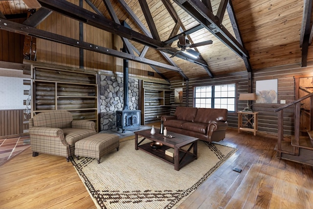 living area with beam ceiling, wood-type flooring, a ceiling fan, a wood stove, and wooden ceiling