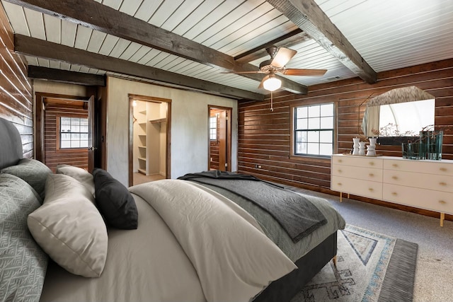 carpeted bedroom featuring a walk in closet, multiple windows, wood walls, and beamed ceiling