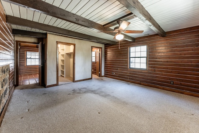 carpeted empty room with beamed ceiling, wooden walls, and ceiling fan