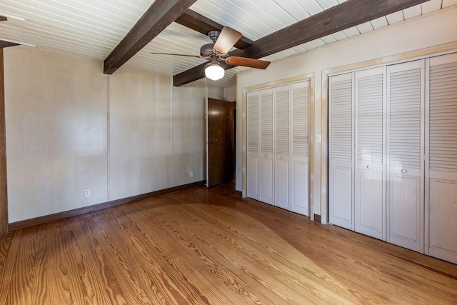 unfurnished bedroom featuring baseboards, light wood-style flooring, ceiling fan, beamed ceiling, and two closets