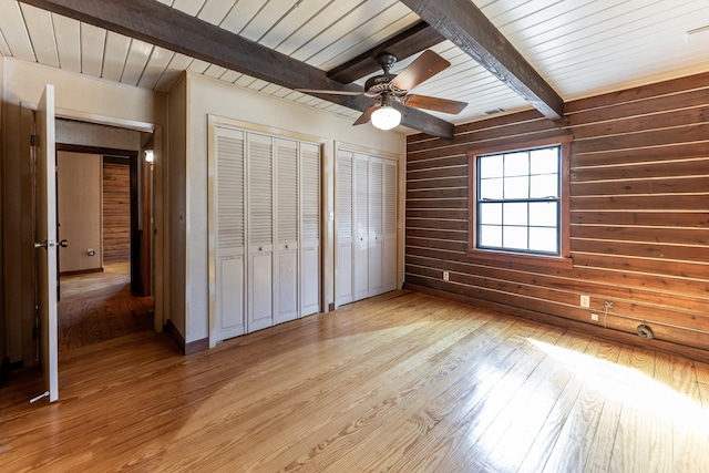 unfurnished bedroom featuring multiple closets, wooden walls, light wood-type flooring, wooden ceiling, and beamed ceiling