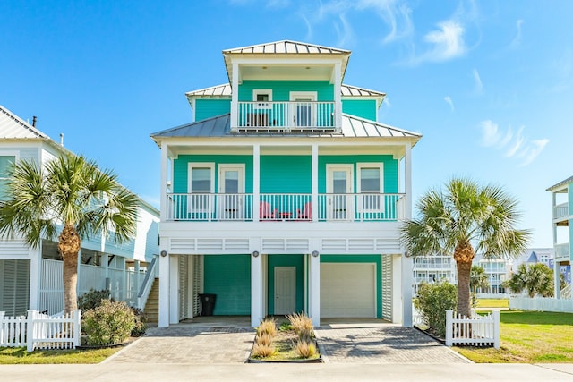 raised beach house with metal roof, a balcony, fence, driveway, and a standing seam roof